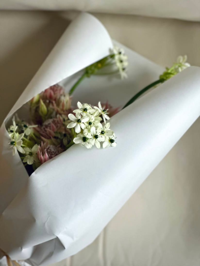 白い紙に包まれた季節のお花のブーケ